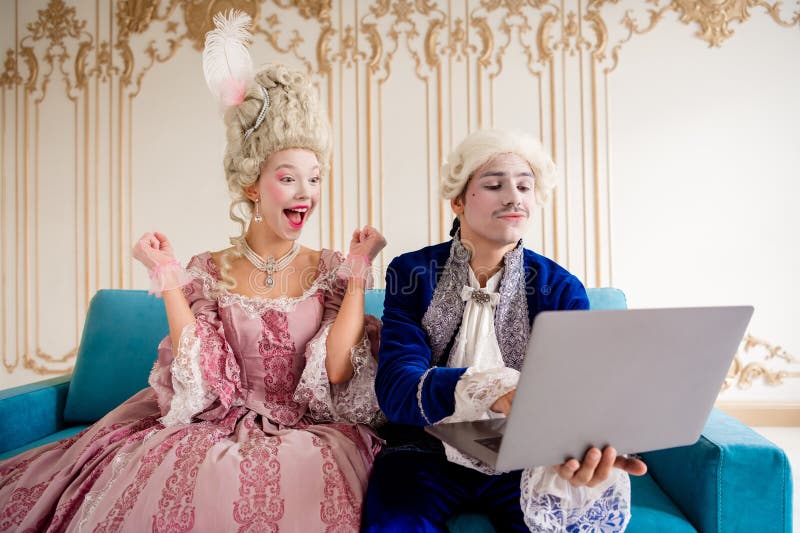 Pareja en trajes barrocos disfrutando del ocio con la tecnología moderna en interiores de inspiración real imagen de archivo libre de regalías