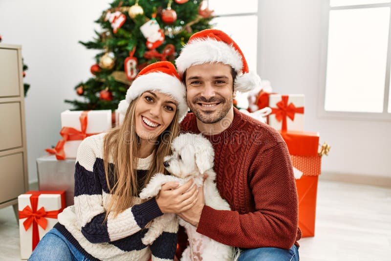 Pareja hispánica joven con sombrero de navidad sentada en el suelo con perro en casa foto de archivo libre de regalías