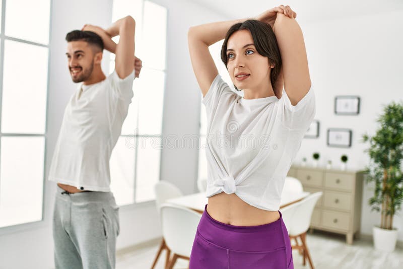 Pareja joven hispana haciendo deporte estirando brazos en casa imagen de archivo