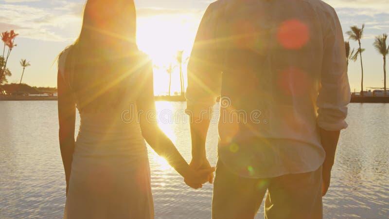 Pareja romántica al atardecer tomándose de la mano en la playa mirando las vacaciones al atardecer