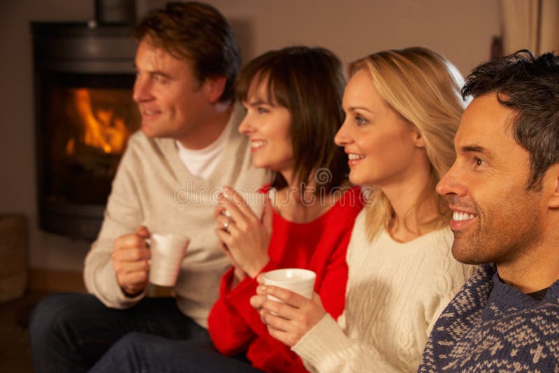 Group Of Middle Aged Couples Sitting On Sofa With Hot Drinks Watching TV. Group Of Middle Aged Couples Sitting On Sofa With Hot Drinks Watching TV