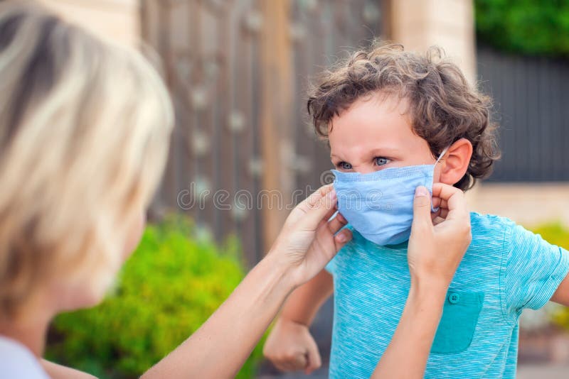Parent with kid in face mask outdoor. Mother helping angry child to wear facemask during coronavirus and flu outbreak. Virus and illness protection