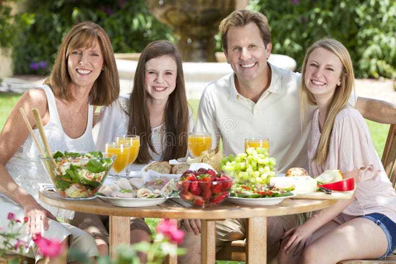 Parents Children Family Healthy Eating Outside. An attractive happy, smiling family of mother, father and two daughters eating healthy food at a table outside stock photo
