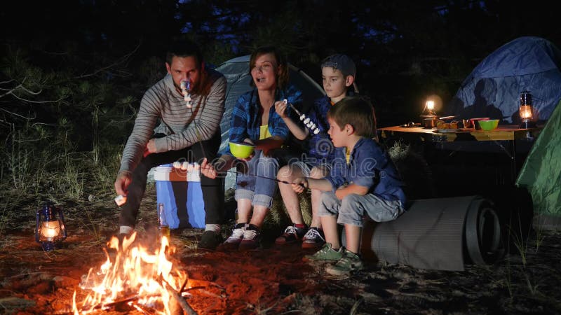 Parents with childs broil marshmallow on campfire to woodland, happy family fry marshmallow at fire