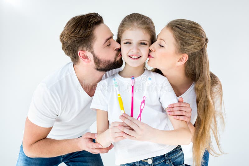 Parents embrassant la petite fille mignonne tenant des brosses à dents photographie stock libre de droits Parents embrassant la petite fille mignonne tenant des brosses à dents photographie stock libre de droits