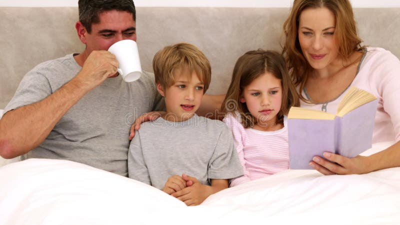 Parents et enfants de sourire lisant ensemble dans le lit