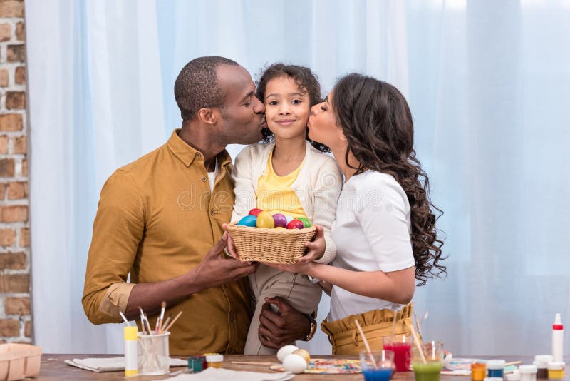 Parents kissing daughter and holding straw basket with easter eggs