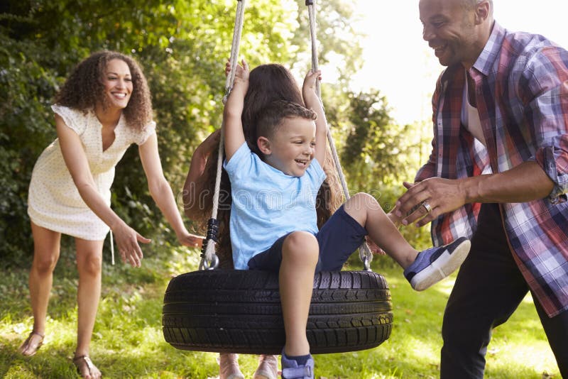 Parents Pushing Children On Tire Swing In Garden