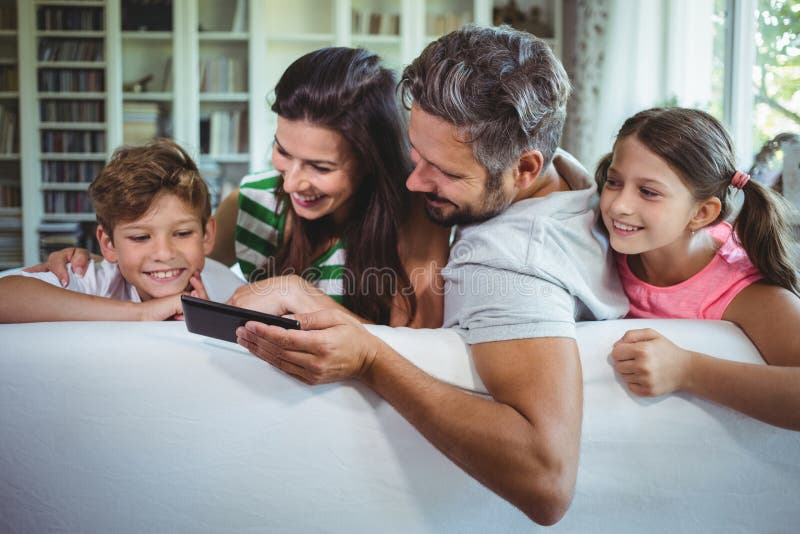 Parents sitting on sofa with their children and using mobile phone in living room