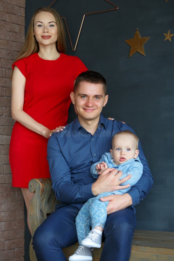 Parents and their child sitting on a bench. Mom, dad and baby. Portrait of young family. Happy family life. Man was born. On gray