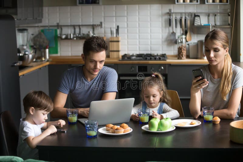 Parents à l'aide de l'ordinateur portable et des smartphones prenant le petit déjeuner avec l'enfant photographie stock Parents à l'aide de l'ordinateur portable et des smartphones prenant le petit déjeuner avec l'enfant photographie stock