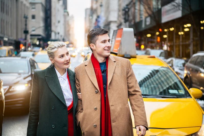Pares adultos jovenes felices que salen del taxi amarillo en la calle de New York City y que miran al lado foto de archivo libre de regalías Pares adultos jovenes felices que salen del taxi amarillo en la calle de New York City y que miran al lado foto de archivo libre de regalías
