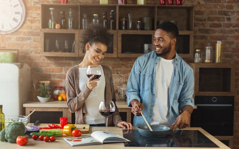 Pares afroamericanos que cocinan la cena y que beben el vino rojo fotografía de archivo Pares afroamericanos que cocinan la cena y que beben el vino rojo fotografía de archivo