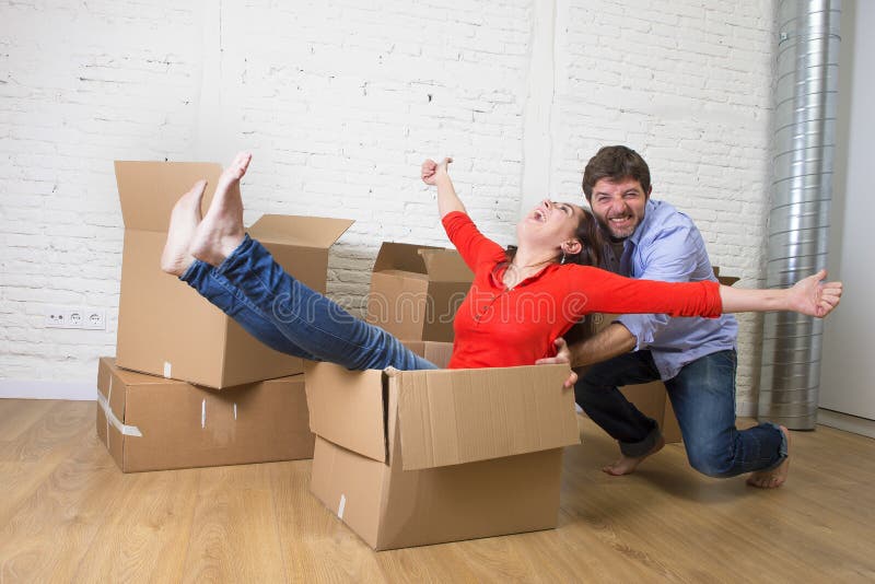 Pares americanos felices que desempaquetan la mudanza en la nueva casa que juega con imagen de archivo Pares americanos felices que desempaquetan la mudanza en la nueva casa que juega con imagen de archivo