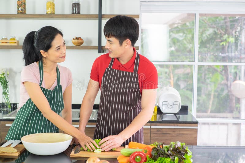 Pares asiáticos Ambos olham os olhos de cada um cozinhando assim o divertimento junto na cozinha com o completo do ingrediente na imagem de stock royalty free Pares asiáticos Ambos olham os olhos de cada um cozinhando assim o divertimento junto na cozinha com o completo do ingrediente na imagem de stock royalty free