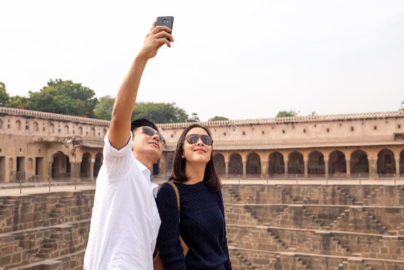 Pares asiáticos felices en el amor que toma la foto del selfie en el stepwell de Chand Baori en la India fotos de archivo libres de regalías Pares asiáticos felices en el amor que toma la foto del selfie en el stepwell de Chand Baori en la India fotos de archivo libres de regalías