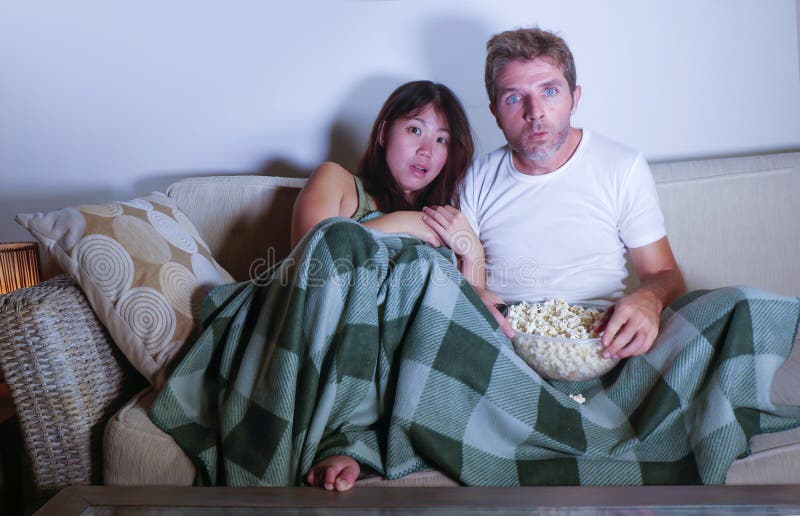 Pares atrativos novos da raça misturada com a mulher coreana asiática e o homem branco que apreciam junto olhar o filme de terror imagens de stock royalty free Pares atrativos novos da raça misturada com a mulher coreana asiática e o homem branco que apreciam junto olhar o filme de terror imagens de stock royalty free