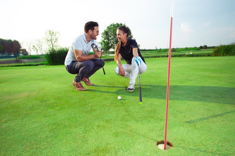 Pares bonitos novos que jogam o golfe na grama imagem de stock Pares bonitos novos que jogam o golfe na grama imagem de stock