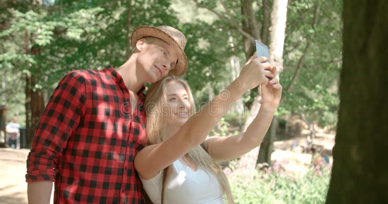 Pares caucasianos novos loving usando o telefone por um lago foto de stock Pares caucasianos novos loving usando o telefone por um lago foto de stock