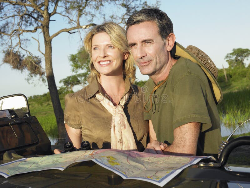 Smiling couple with at map on bonnet of jeep looking at view. Smiling couple with at map on bonnet of jeep looking at view