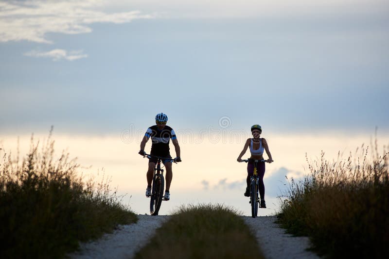 Pares de bicicletas da equitação do ciclista na estrada secundária Jovens aptos no sportswear que dá um ciclo para baixo imagem de stock Pares de bicicletas da equitação do ciclista na estrada secundária Jovens aptos no sportswear que dá um ciclo para baixo imagem de stock