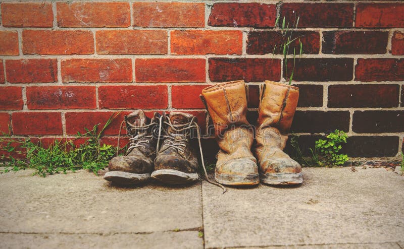 Two pairs of old boots in front of a  brick wall.The boots are heavily worn steel toe cap safety boots. Two pairs of old boots in front of a  brick wall.The boots are heavily worn steel toe cap safety boots.
