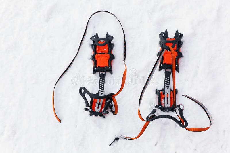 Pair of orange crampons with spikes for mountaineering is on white snow. Pair of orange crampons with spikes for mountaineering is on white snow.