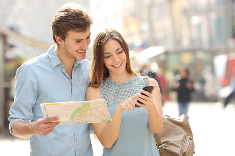 Pares de los turistas que consultan una guía de la ciudad y a los gps del smartphone fotografía de archivo libre de regalías Pares de los turistas que consultan una guía de la ciudad y a los gps del smartphone fotografía de archivo libre de regalías