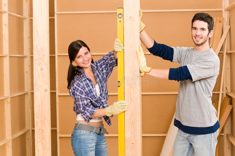 Home improvement smiling young couple fixing wall with spirit level. Home improvement smiling young couple fixing wall with spirit level