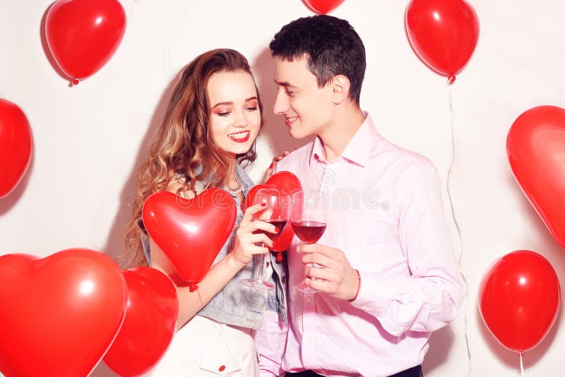 Pares de Valentine Beauty con el vino tinto de consumición de aire del corazón rojo de los balones Abrazos felices hermosos de la fotografía de archivo Pares de Valentine Beauty con el vino tinto de consumición de aire del corazón rojo de los balones Abrazos felices hermosos de la fotografía de archivo