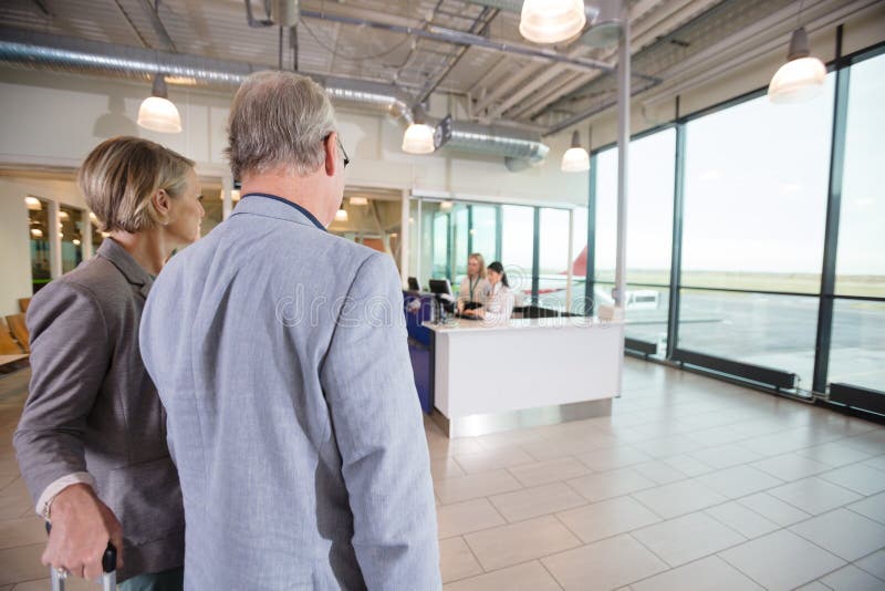 Pares del negocio que miran a los recepcionistas que trabajan en aeropuerto fotografía de archivo Pares del negocio que miran a los recepcionistas que trabajan en aeropuerto fotografía de archivo