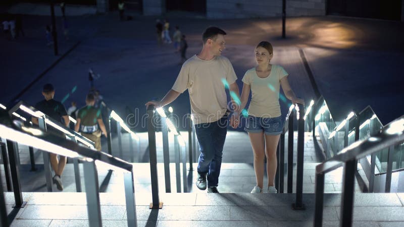 Pares despreocupados que andam em cima para olhar a cidade iluminada da noite, data romântica fotografia de stock Pares despreocupados que andam em cima para olhar a cidade iluminada da noite, data romântica fotografia de stock