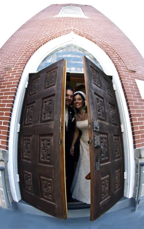 A fish eye shot of a happy wedding peeking out church doors. A fish eye shot of a happy wedding peeking out church doors.