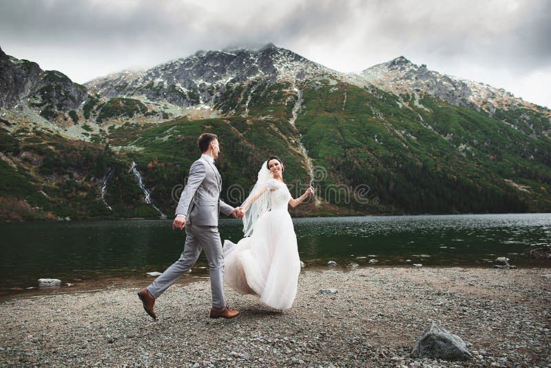 Pares do casamento que correm perto do lago em montanhas de Tatra no Pol?nia Morskie Oko Dia de ver?o bonito imagem de stock royalty free Pares do casamento que correm perto do lago em montanhas de Tatra no Pol?nia Morskie Oko Dia de ver?o bonito imagem de stock royalty free