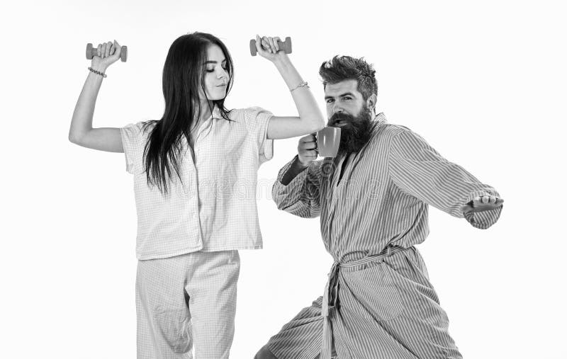 Pares en amor en el pijama, soporte de la albornoz aislado en el fondo blanco Muchacha con pesa de gimnasia, hombre con la taza d imágenes de archivo libres de regalías Pares en amor en el pijama, soporte de la albornoz aislado en el fondo blanco Muchacha con pesa de gimnasia, hombre con la taza d imágenes de archivo libres de regalías