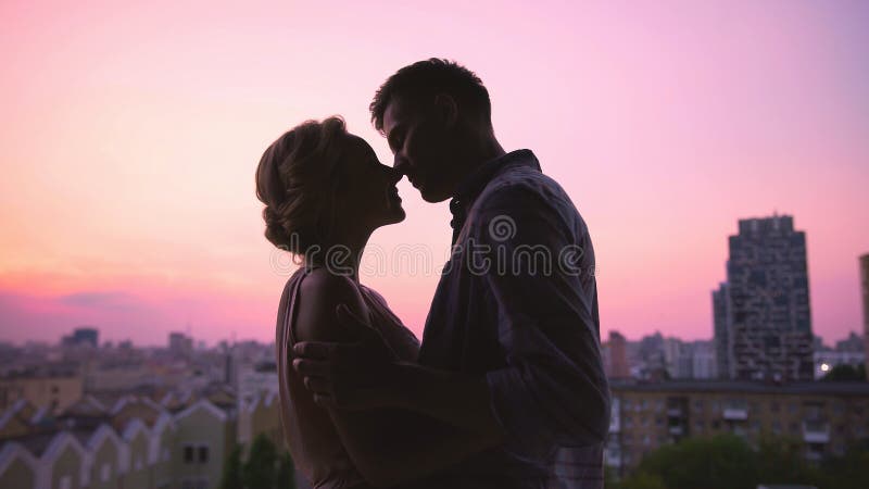 Pares en besarse del amor suavemente, colocándose en el tejado de la casa, puesta del sol hermosa foto de archivo Pares en besarse del amor suavemente, colocándose en el tejado de la casa, puesta del sol hermosa foto de archivo
