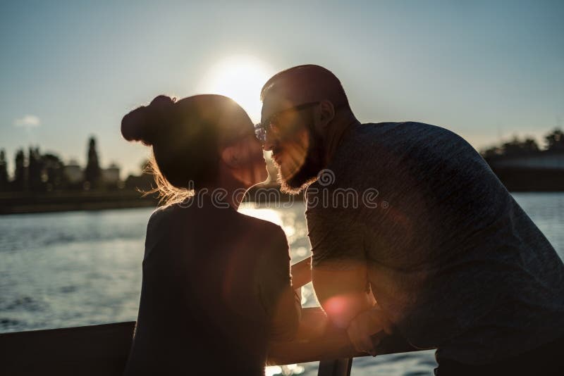 Pares en el amor que se besa por el río en la puesta del sol fotografía de archivo Pares en el amor que se besa por el río en la puesta del sol fotografía de archivo