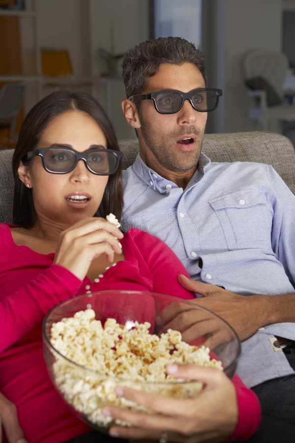 Pares en Sofa Watching TV que lleva los vidrios 3D que comen las palomitas imágenes de archivo libres de regalías Pares en Sofa Watching TV que lleva los vidrios 3D que comen las palomitas imágenes de archivo libres de regalías