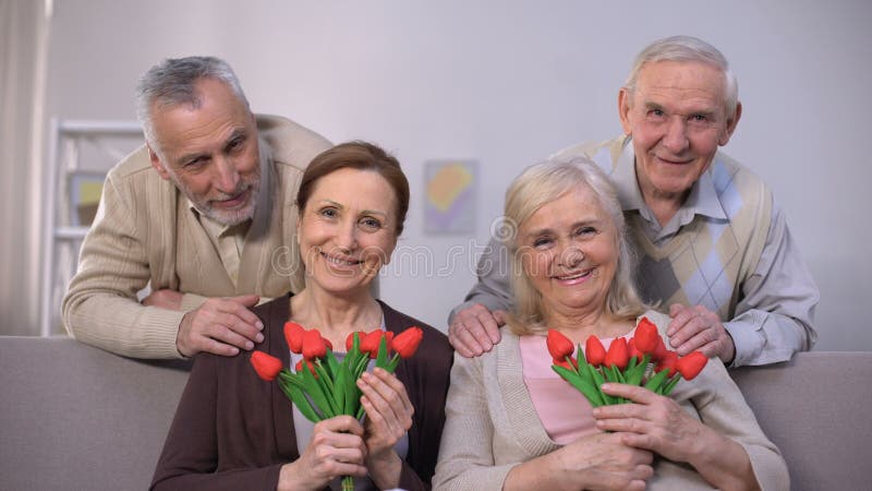 Pares envejecidos que abrazan y que sonríen en la cámara, mujeres que sostienen los tulipanes, celebración
