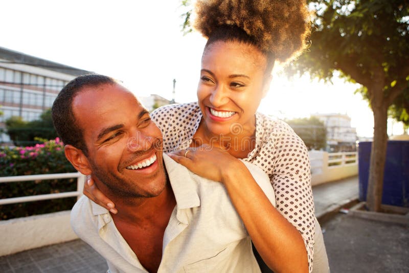 Pares felices con la mujer que lleva del hombre en ciudad fotos de archivo libres de regalías Pares felices con la mujer que lleva del hombre en ciudad fotos de archivo libres de regalías
