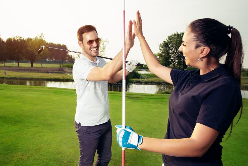 Pares felices del jugador de golf que dan el alto cinco mientras que se coloca en campo foto de archivo libre de regalías Pares felices del jugador de golf que dan el alto cinco mientras que se coloca en campo foto de archivo libre de regalías