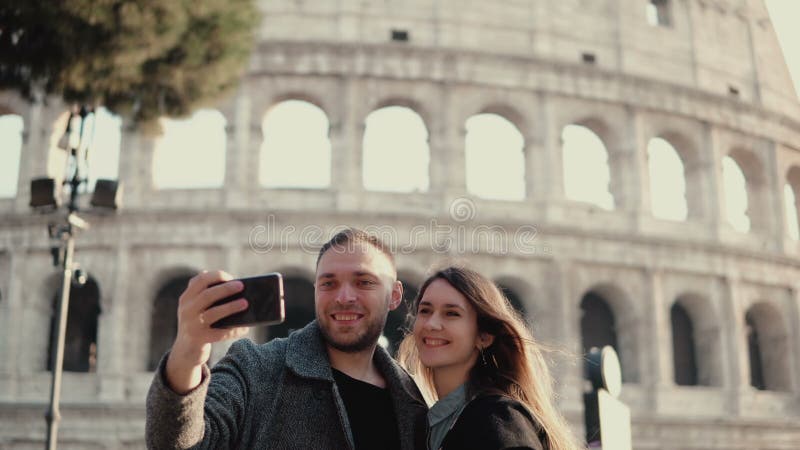 Pares felices jovenes que viajan en Roma, Italia Hombre y mujer que toman la foto del selfie en smartphone cerca del Colosseum fotografía de archivo Pares felices jovenes que viajan en Roma, Italia Hombre y mujer que toman la foto del selfie en smartphone cerca del Colosseum fotografía de archivo