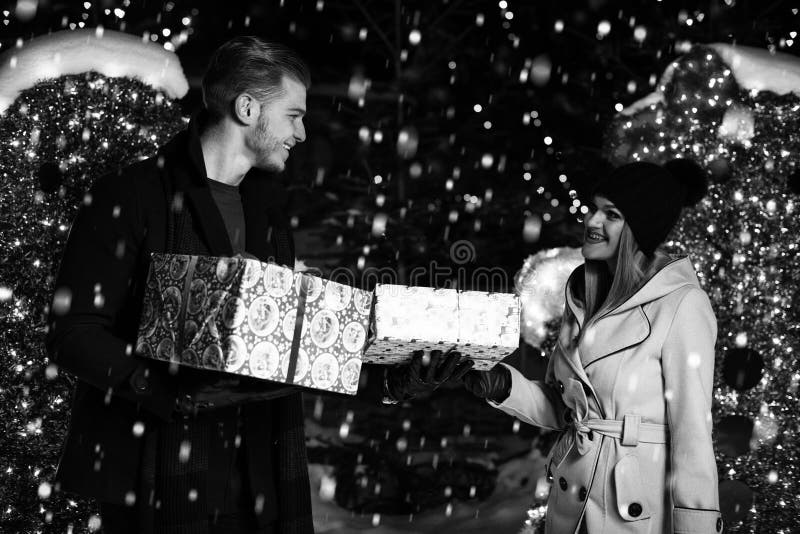 Pares felizes com a caixa de presente sobre luzes de Natal foto de stock Pares felizes com a caixa de presente sobre luzes de Natal foto de stock