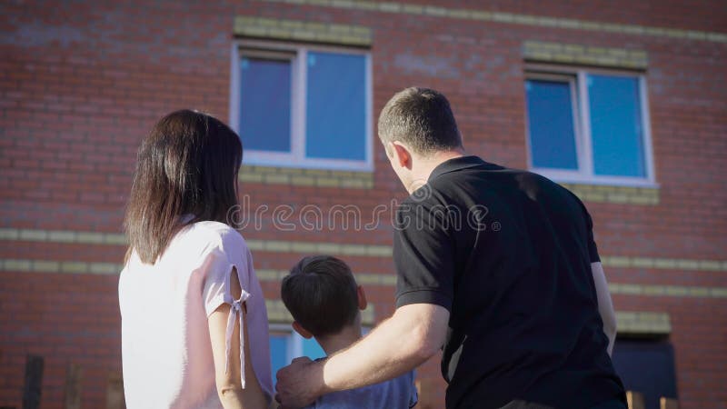 Pares felizes com a criança que olha o apartamento novo Família loving no dia ensolarado do verão que mostra a menino a casa mode