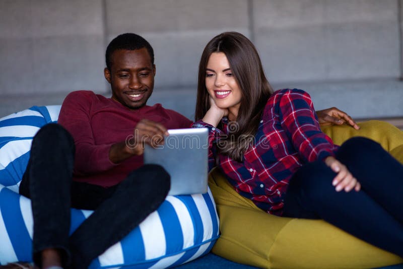 Pares felizes com tabuleta e smartphone do computador em um sof? imagem de stock Pares felizes com tabuleta e smartphone do computador em um sof? imagem de stock