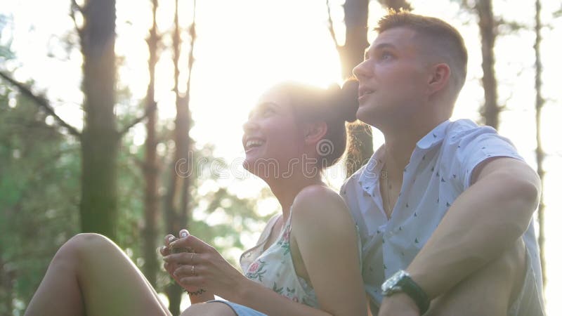 Pares felizes do moderno que penduram para fora no parque no por do sol