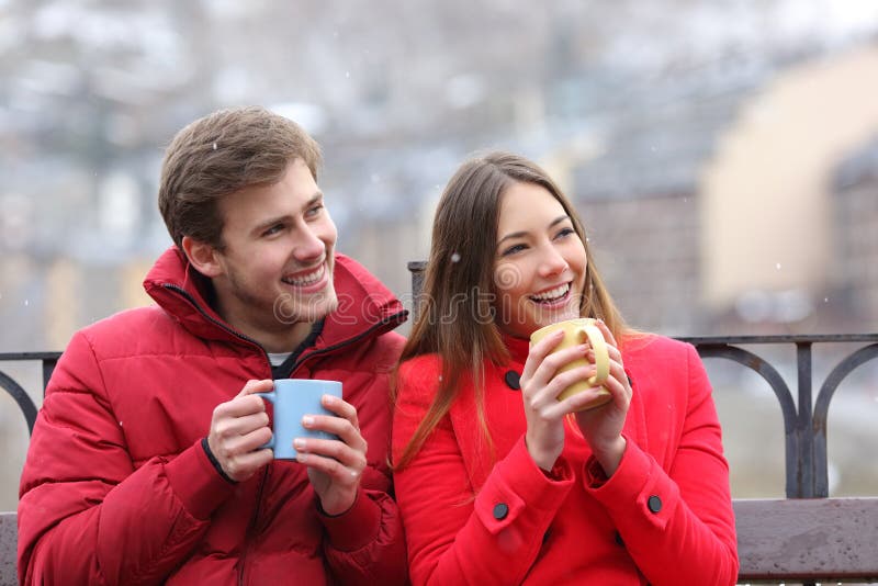 Pares felizes que bebem as bebidas quentes que olham o lado no inverno fotos de stock Pares felizes que bebem as bebidas quentes que olham o lado no inverno fotos de stock
