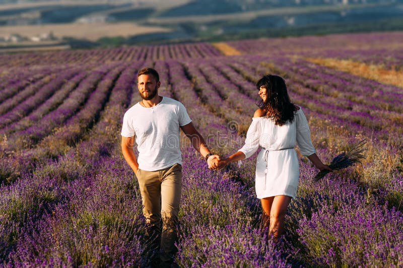 Pares felizes que guardam as mãos em campos da alfazema Pares no amor em campos de flor Viagem da lua de mel Siga-me Pares bonito fotos de stock Pares felizes que guardam as mãos em campos da alfazema Pares no amor em campos de flor Viagem da lua de mel Siga-me Pares bonito fotos de stock