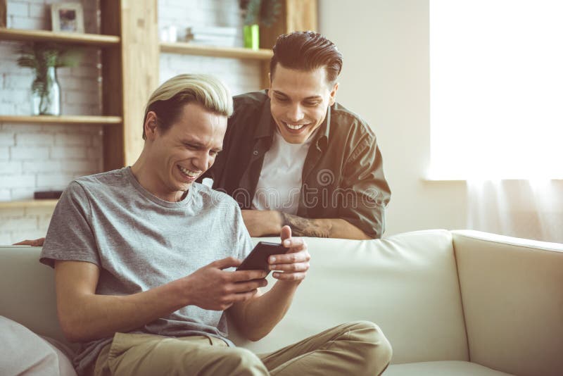 Pares gay alegres que miran los vídeos divertidos en smartphone fotografía de archivo Pares gay alegres que miran los vídeos divertidos en smartphone fotografía de archivo