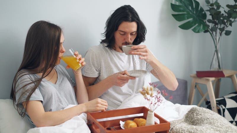 Pares hermosos que desayunan en cama en casa con los pasteles del zumo de fruta del café